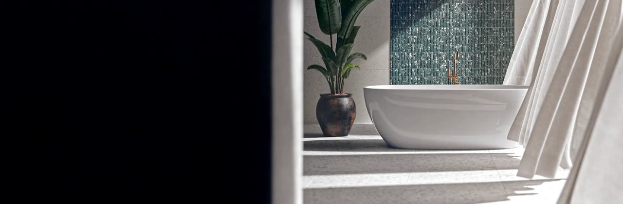 Modern bathroom with a white freestanding bathtub, brass floor-mounted bath filler and a green glass mosaic tile feature wall.