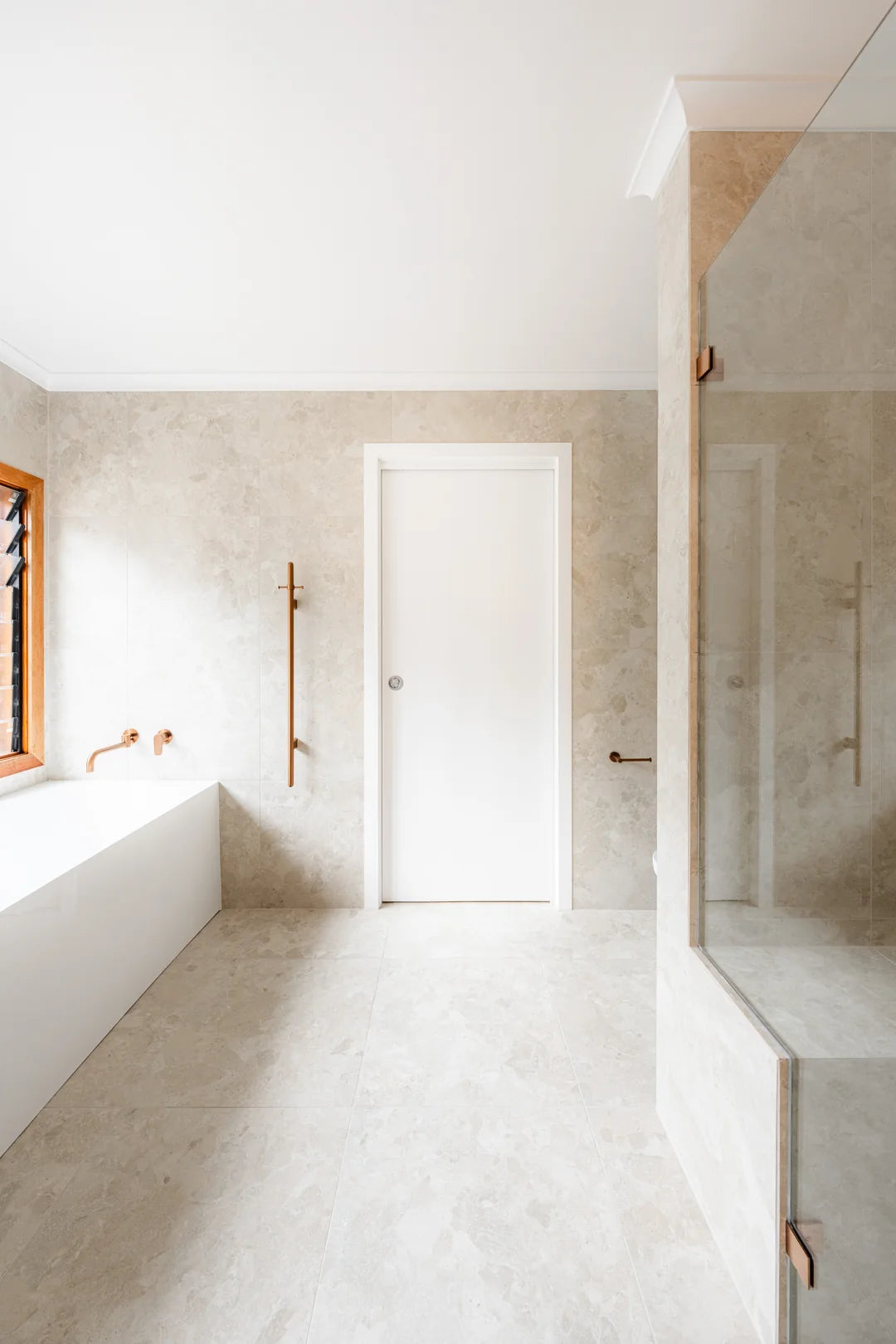 Pale tiled bathroom floor beside a bath and glass shower